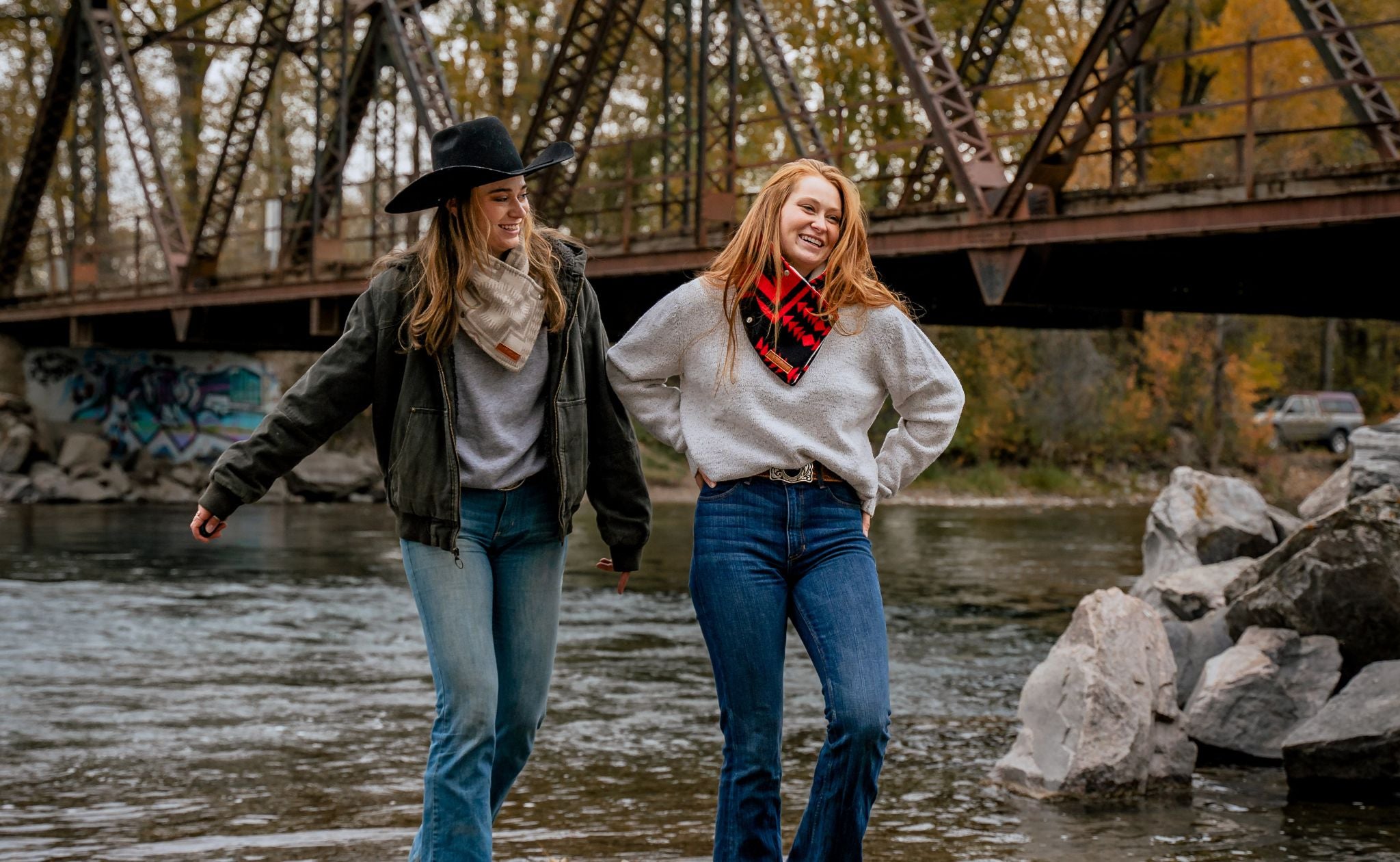 Two women in western fashion clothing and Pendleton wool scarves walk along the Gallatin river in bozeman montana..